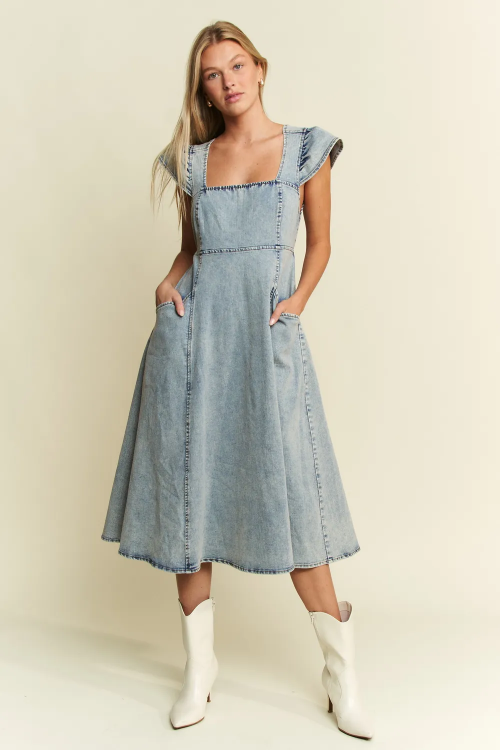 Woman wearing a denim dress with white boots on a plain background


